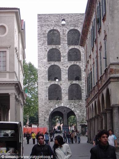 Porta Soprana in Genoa, medieval stone towers between buildings, pedestrians under the arch