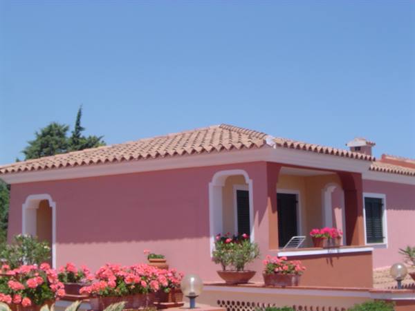 Pink house with tiled roof, blooming geraniums and clear blue sky