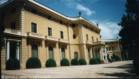 Yellow 19th-century villa with columns and round hedges by the entrance