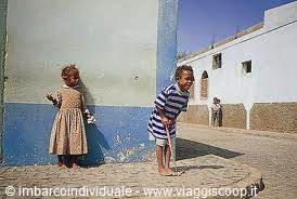 Children play beside blue and white walls in a sunny alley