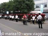 Red tourist train stopped on the street, people queueing under the trees