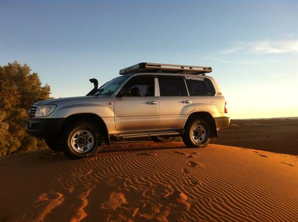Silver Toyota Land Cruiser on a sand dune in the desert at sunset