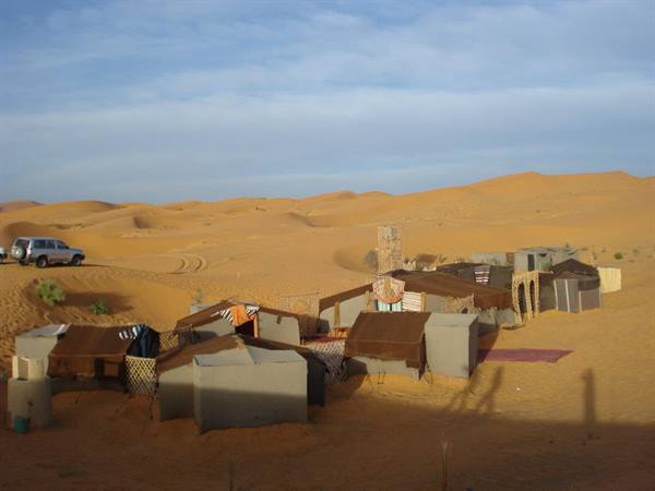 Berber camp with dark fabric tents among Erg Chebbi dunes, parked 4x4