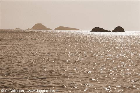 Sun glitters on the sea in front of dark islets