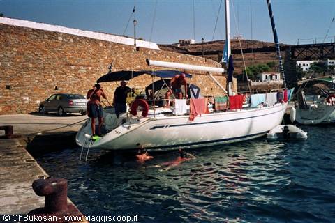 Sailing yacht moored by stone wall, people on deck, laundry hanging