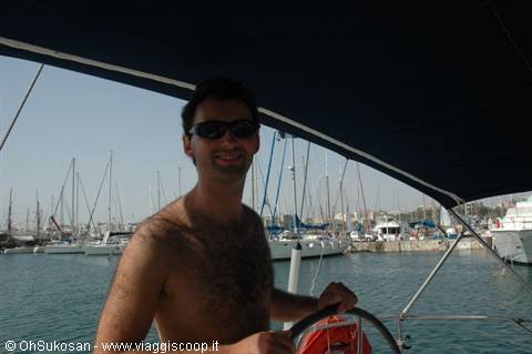 Man in sunglasses steering a sailboat inside the marina