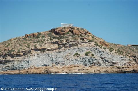 Rocky hill above blue sea with white sign on top