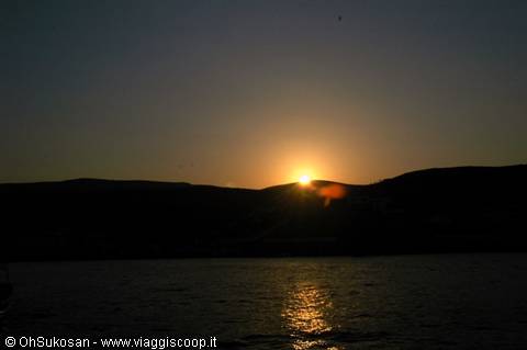 Sun rising behind dark hills, golden light reflecting on the sea