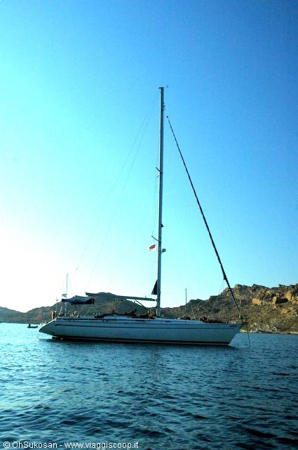 White sailboat anchored in a rocky cove, blue sky and calm sea