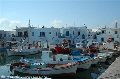Colorful fishing boats moored at Naoussa harbor, whitewashed Cycladic houses behind