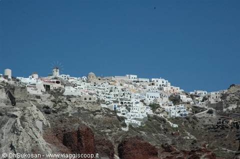 White houses carved in red rock, windmill, blue sky, Oia