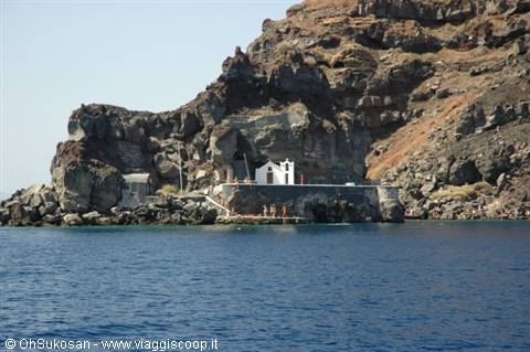 Small white chapel on dark volcanic rocks beside deep blue sea
