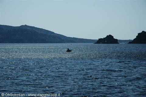 Fisher on a small boat at sea near black rocks and hills
