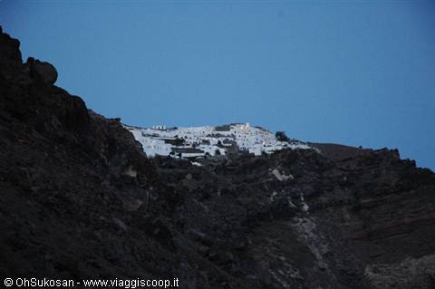 White village glowing on dark volcanic rock, Santorini at dusk