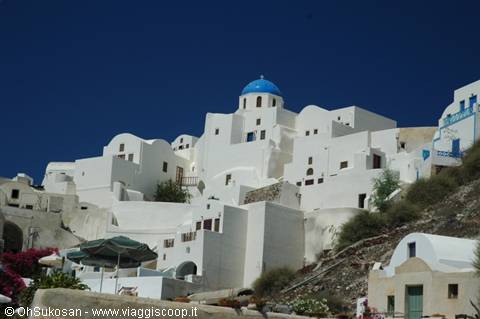 White church with blue dome among Oia's houses, bright sunlight