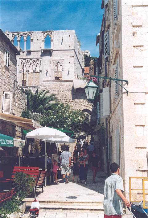 Tourists in a stone alley with cafés under umbrellas and Gothic palace, Dubrovnik