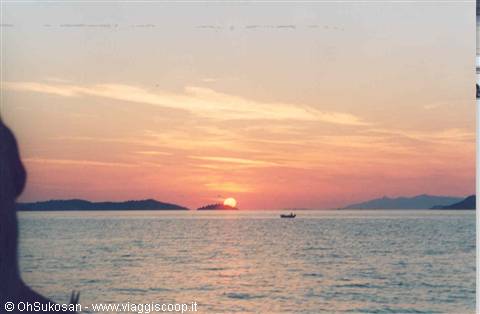 Orange sun sinking over the sea before dark islets, small rowing boat
