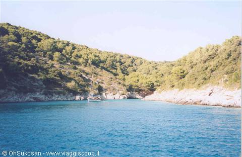 Sailboat anchored in turquoise bay between rocky shores and green Mediterranean scrub