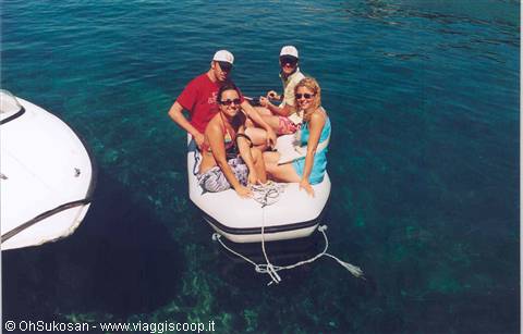 Four friends on an inflatable dinghy in turquoise water beside a white boat