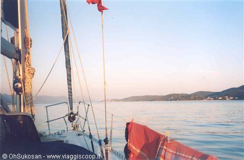 Sailboat bow at anchor, towels drying, coastline ahead in soft light