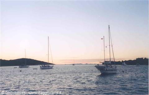 Sailboats anchored in a calm bay at dusk, pale sky over the water