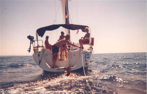 Boy dives into the sea from the sailboat, friends on deck