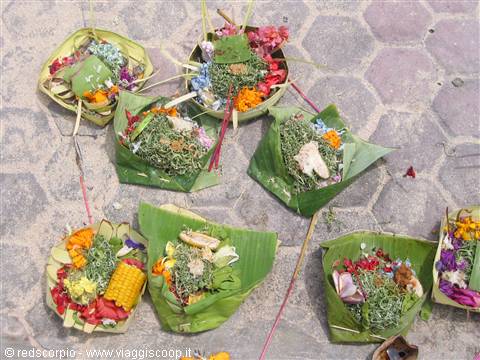 Balinese canang offerings of banana leaves, flowers and rice on stone pavement
