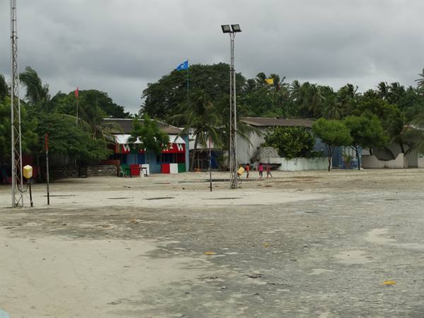 Sandy beach with colorful houses, palm trees and lampposts under cloudy sky