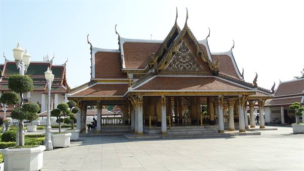 Thai pavilion with ornate golden roof, red tiles, white columns, paved courtyard