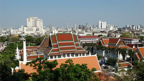 Red temple roofs among green trees, Bangkok skyscrapers rising in the background