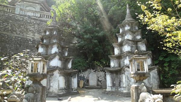 Two weathered stone stupas among greenery, sunlight filtering through trees