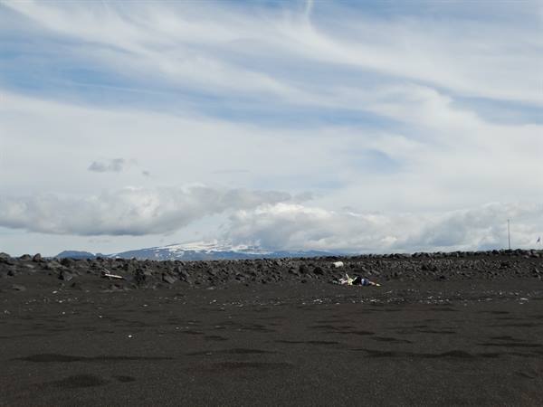 Black volcanic sand beach, dark rocks and snow-capped volcano under clouds
