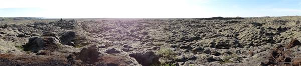 Rugged black lava field under bright sky, barren volcanic terrain