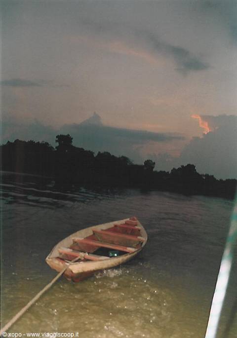 Wooden boat towed on dark river by trees under cloudy sky