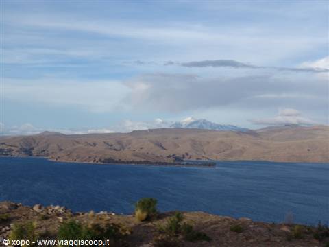 Blue lake at the foot of the Andes, arid hills and snowy peaks among clouds