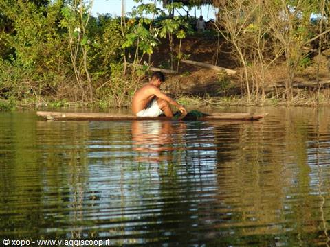 Man paddling wooden dugout canoe on river, golden light through trees