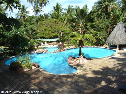 Pool among palms and rocks, with thatched huts, under the sun