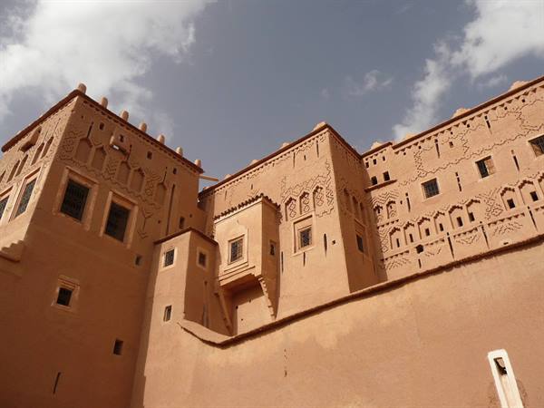 Earthen kasbah with carved decorations, cloudy sky, natural light