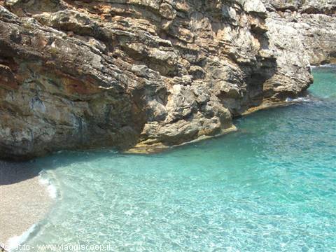 Clear turquoise water between rocky cliffs and a small pebble beach