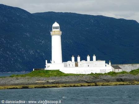 White lighthouse with keeper's cottages on rocky islet, dark mountains behind