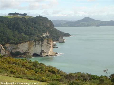 White limestone cliffs above turquoise bay, green hills, Coromandel