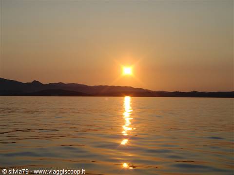 Low sun reflecting on calm water, dark mountains silhouetted against golden sky
