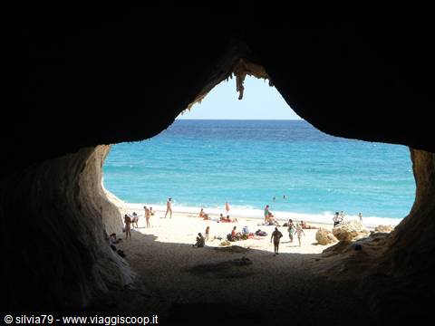 Beach seen from inside a limestone cave, swimmers and turquoise sea, Cala Luna