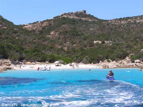 Jet ski gliding across turquoise water in front of granite beach and green hills