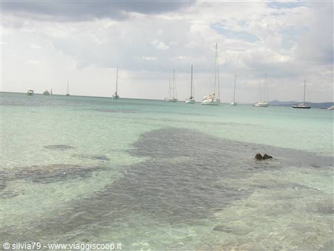 Sailboats anchored in clear turquoise water under cloudy sky