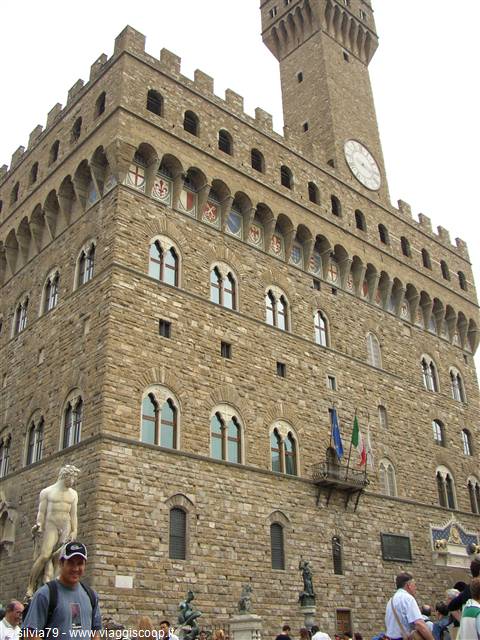 Palazzo Vecchio in Florence, stone facade with battlements, clock tower, flags