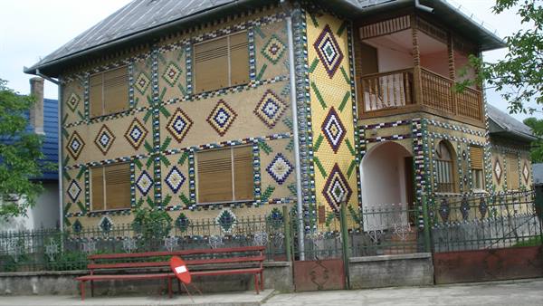 Two-story house covered in colorful geometric pebble mosaic, red bench in front