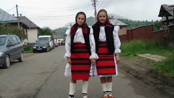 Two girls wearing traditional Romanian dress with red and black skirts on a village road