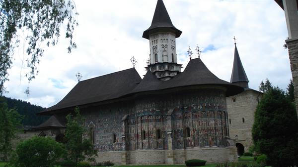 Sucevița painted monastery, exterior frescoes and dark roof among the trees