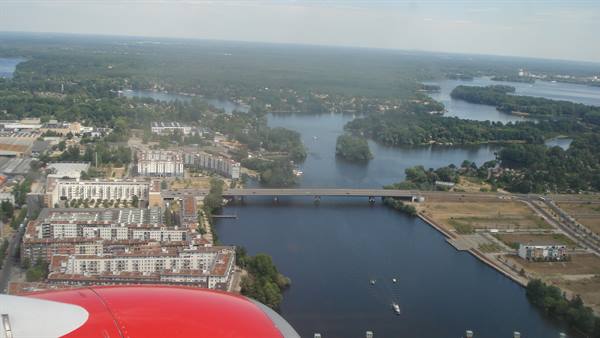 Red airplane engine above river, bridge and buildings among lakes